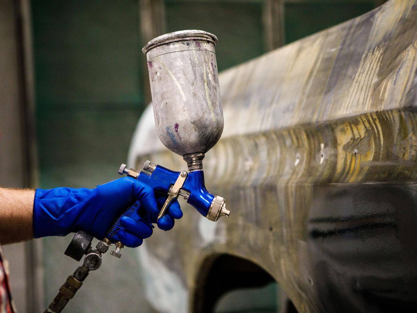 Spray gun laying primer down a stripped panel in the booth