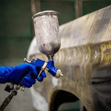 Close up of a gravity feed spray gun over a prepped panel