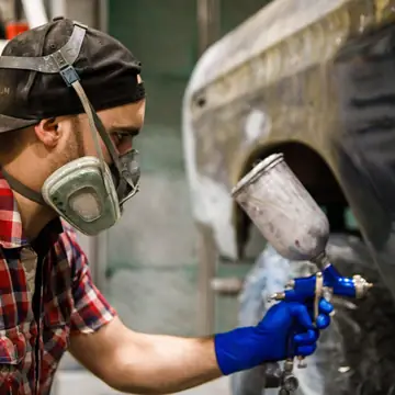 Painter spraying a stripped quarter panel in the booth